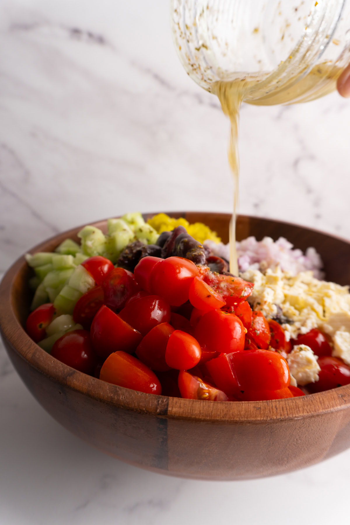 Pouring dressing over the top of a Greek couscous salad.