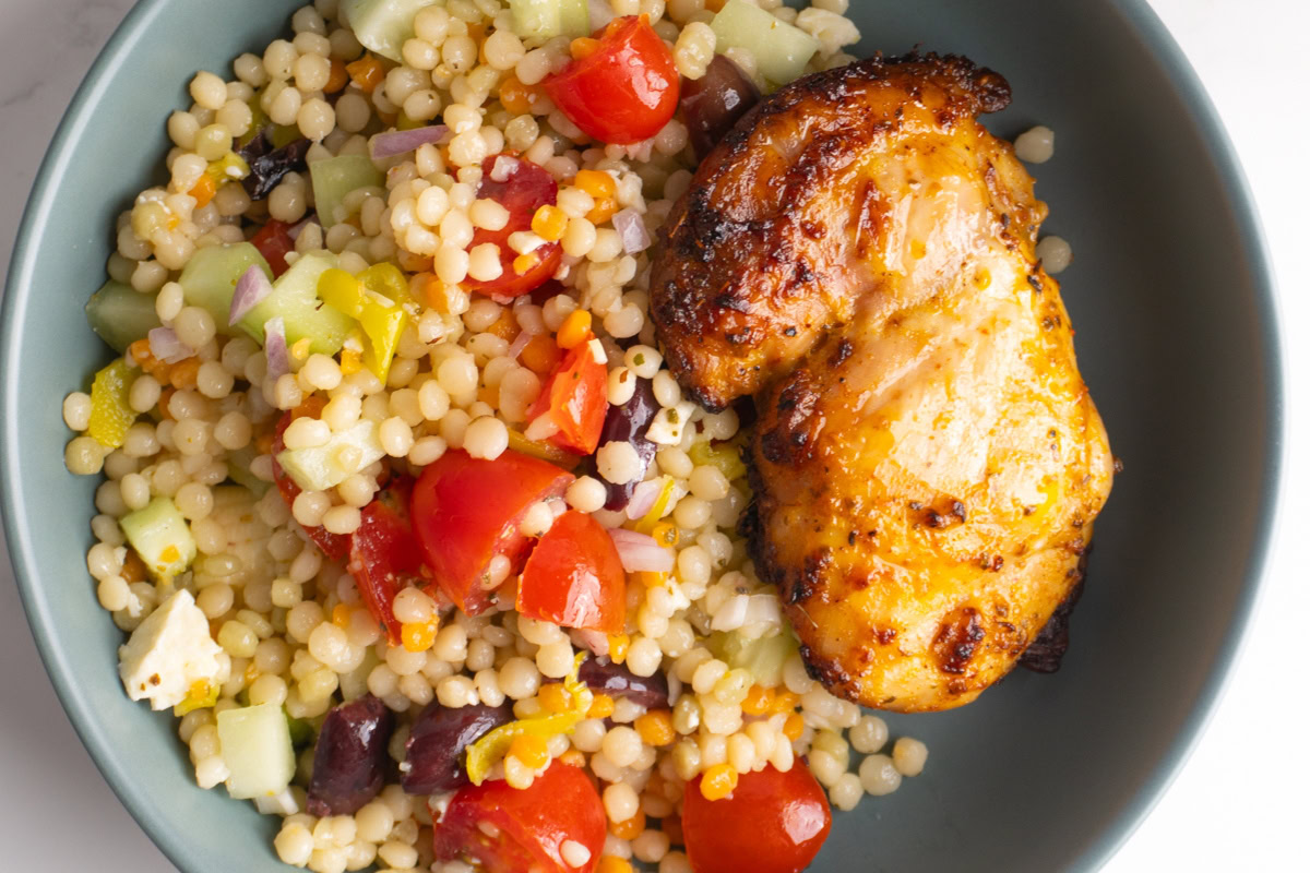 Close up of a Greek couscous salad in a bowl with chicken on the side.