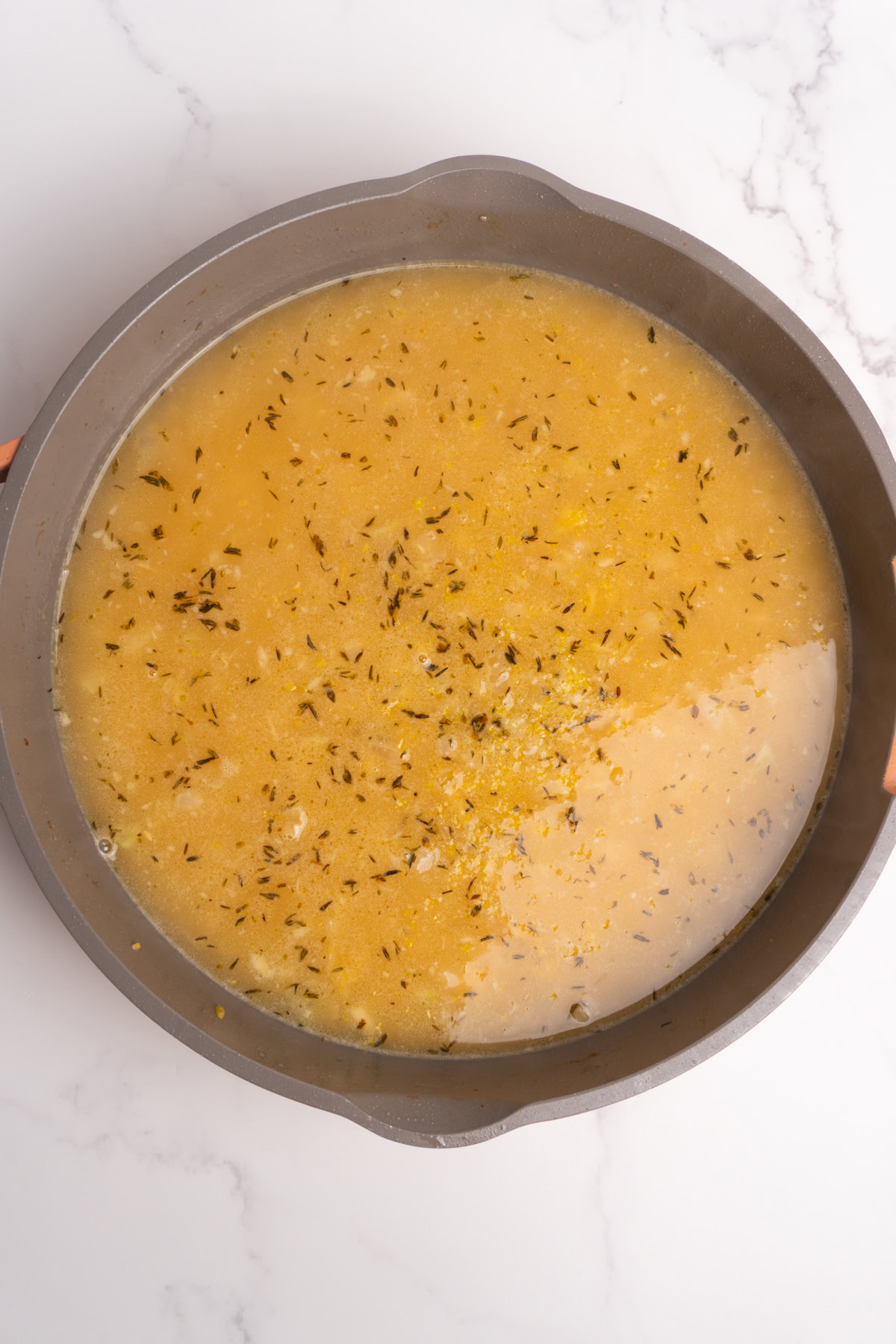 Broth and lemon juice added to the orzo in a skillet.