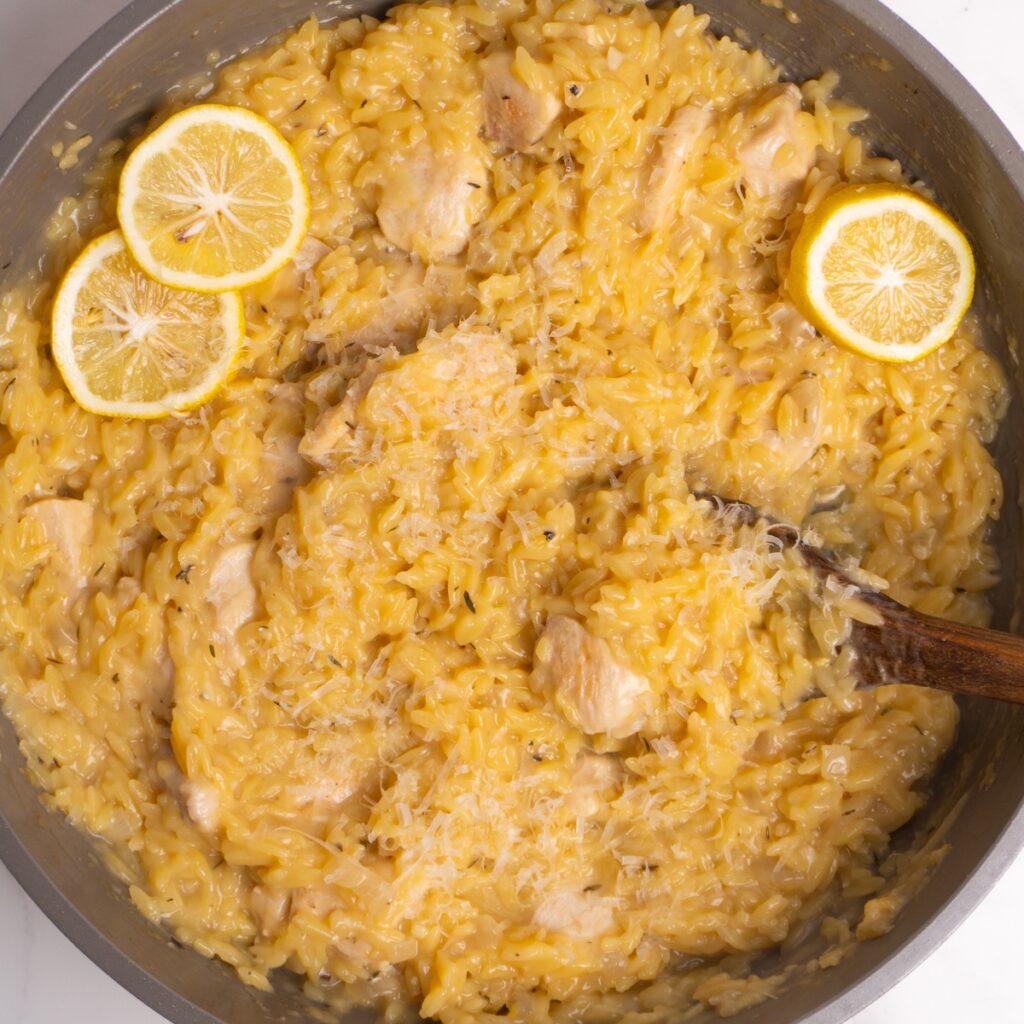 Overhead shot of lemon chicken orzo topped with parmesan and lemon slices.