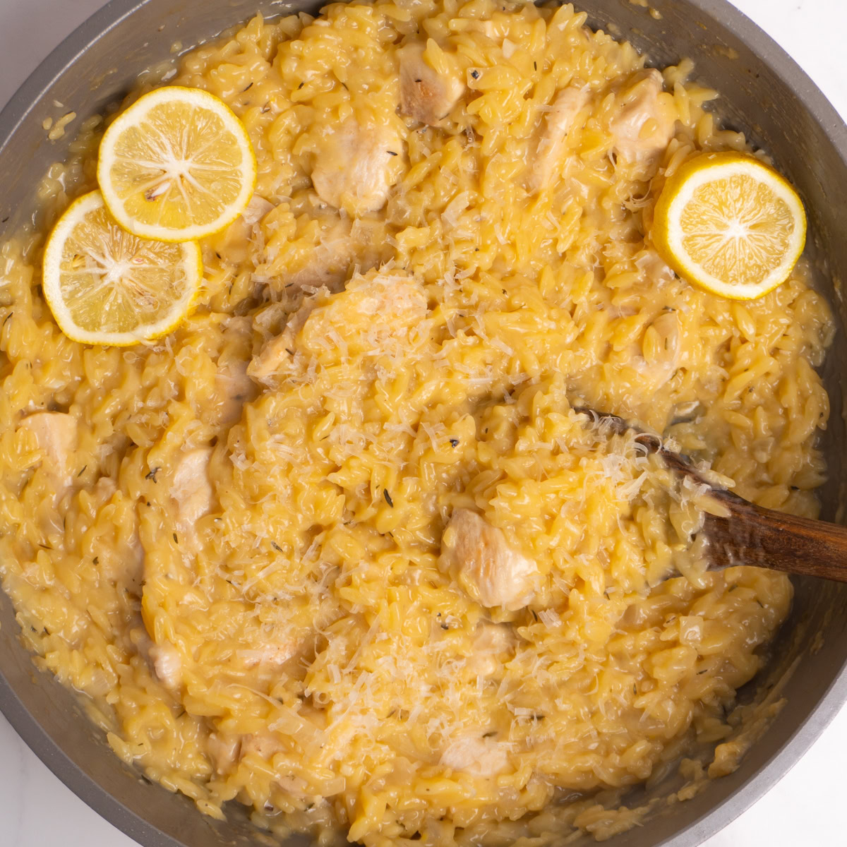 Overhead shot of lemon chicken orzo topped with parmesan and lemon slices.